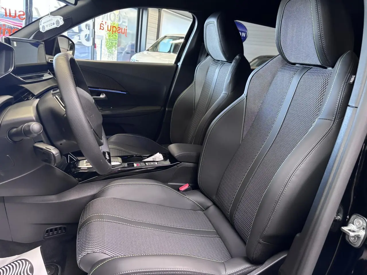 Vue intérieure côté conducteur du Peugeot 2008 1.2i Hybrid 2026, sièges tissu et cuir noir avec surpiqûres vertes.