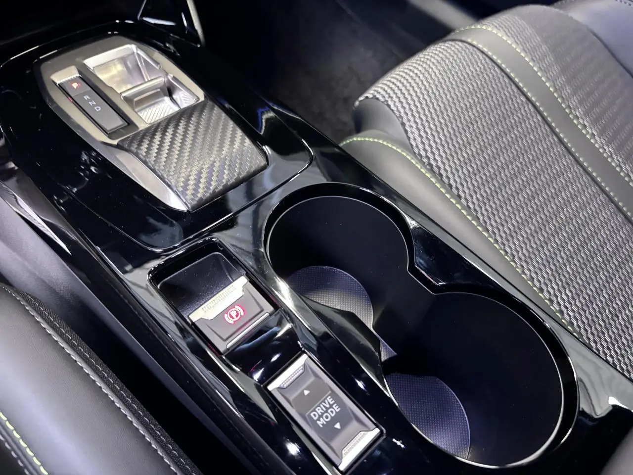 Gros plan sur la console centrale noire brillante avec sélecteur de boîte auto et bouton Drive Mode, siège tissu gris avec surpiqûres vertes.