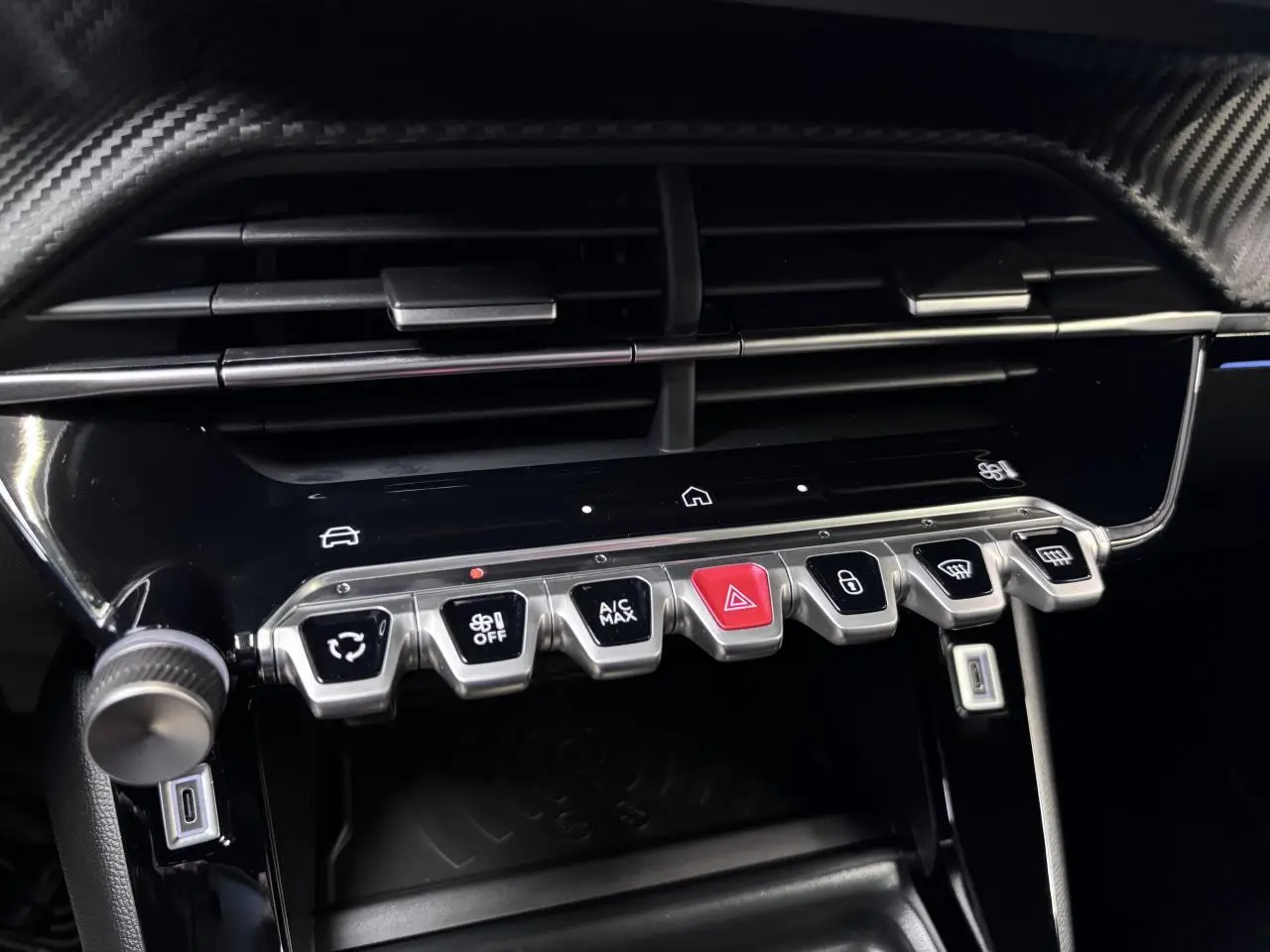 Gros plan sur la console centrale du Peugeot 2008 1.2i Hybrid GT 2026, avec commandes climatisation et finition carbone.