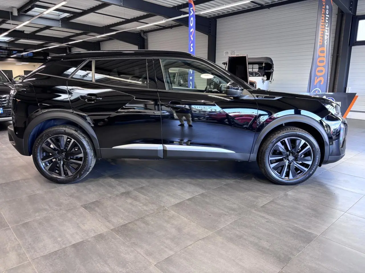 Profil droit d’un Peugeot 2008 noir brillant avec jantes alliage bi-ton 18’’ dans un showroom intérieur.
