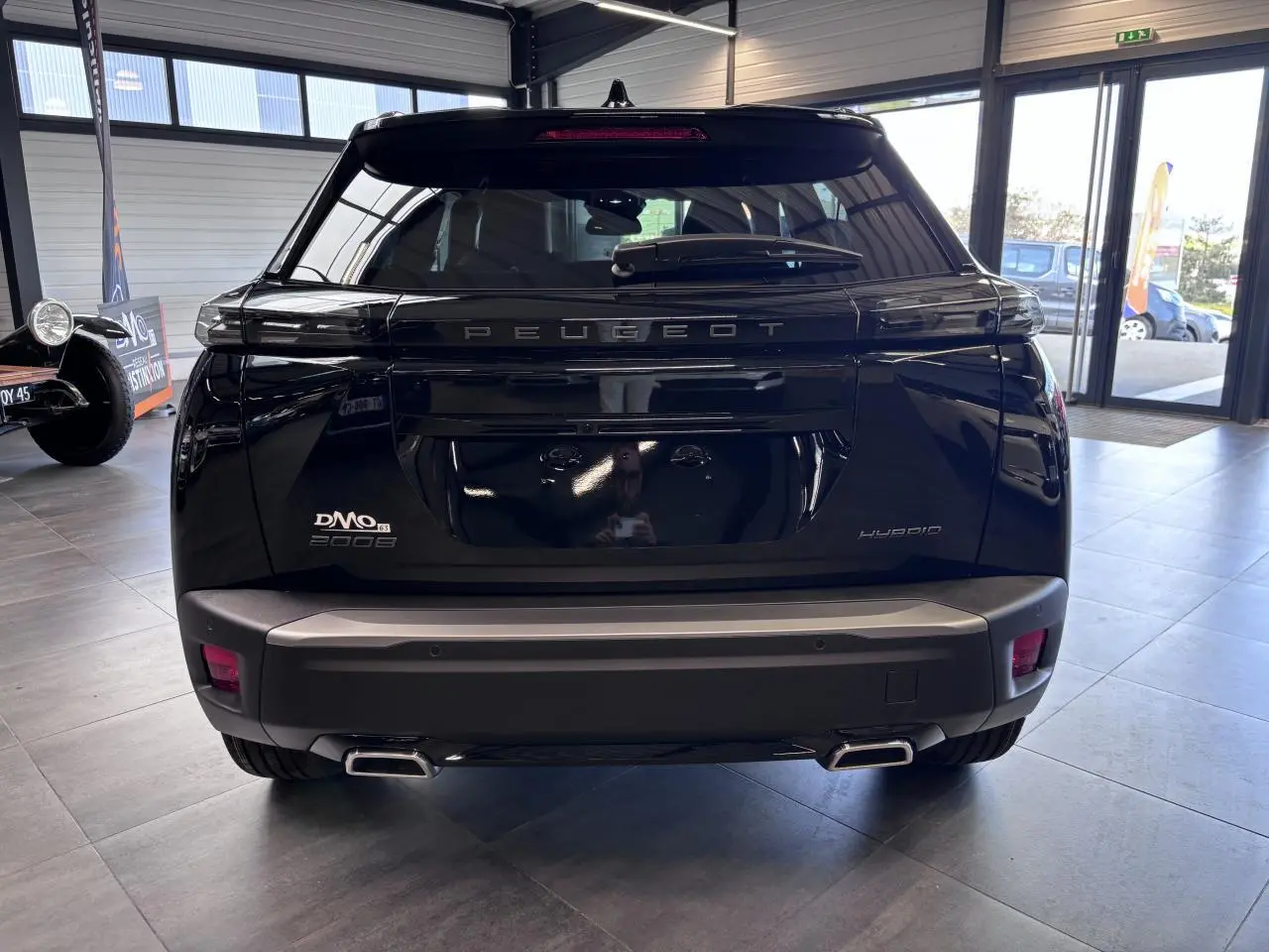Vue arrière d'un Peugeot 2008 hybride noire, avec double sortie d'échappement et logo PEUGEOT en relief sur le hayon.
