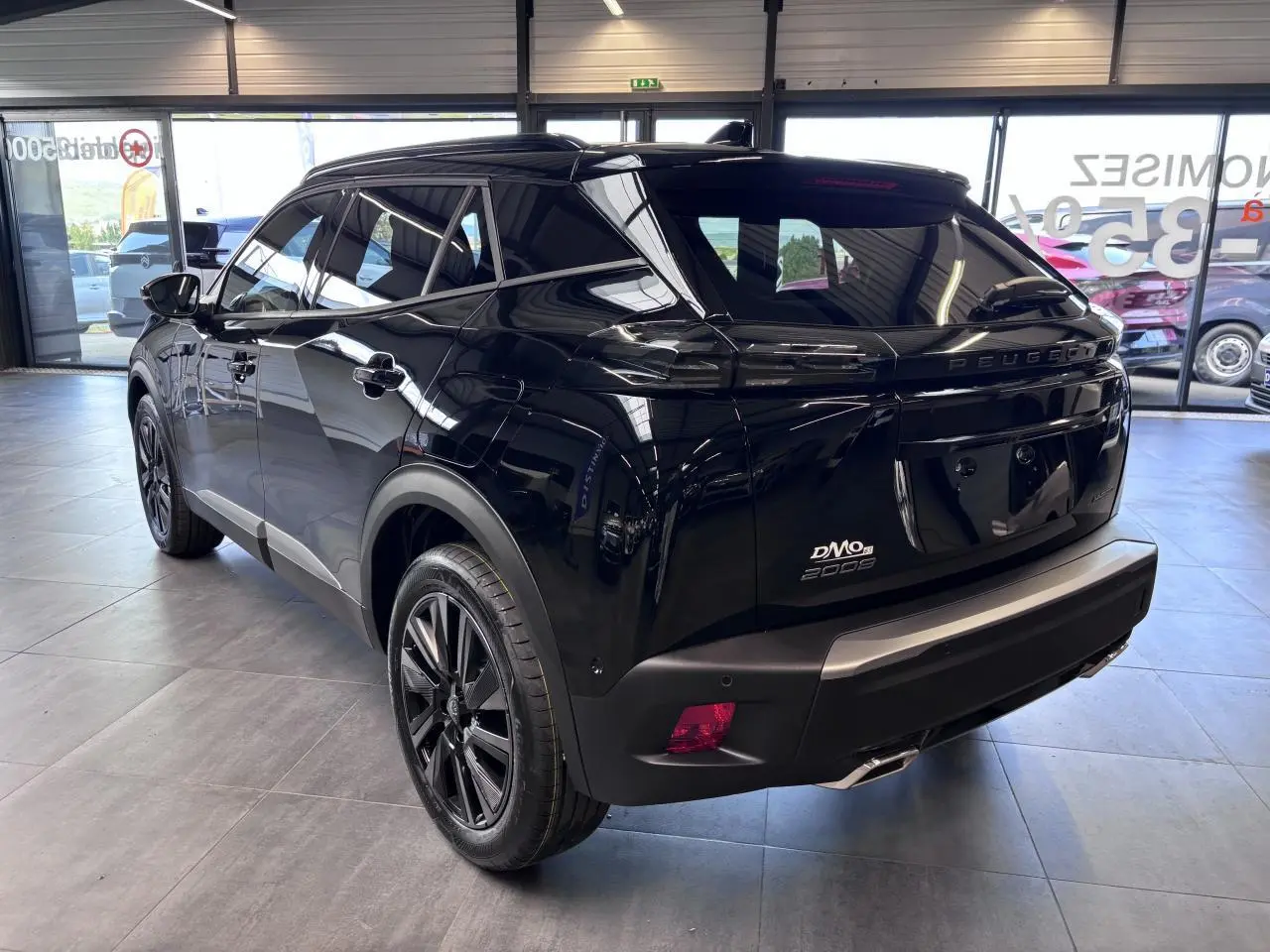 Vue 3/4 arrière droite d'un Peugeot 2008 noir brillant avec jantes alliage 18'' bi-tons dans un showroom.