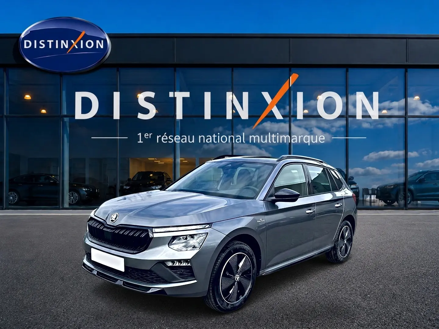 Skoda Kamiq gris graphite en 3/4 avant droit, avec jantes alu noires et toit panoramique visible.