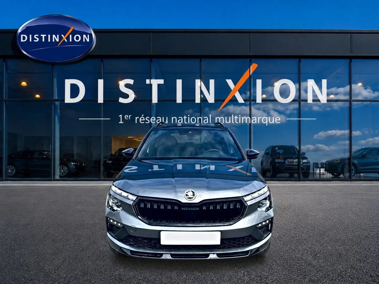 Vue frontale d'un Skoda Kamiq gris graphite garé devant une vitrine avec logo Distinxion en arrière-plan.