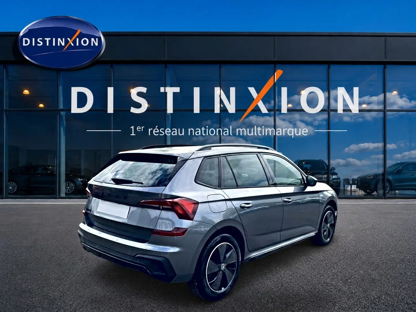 Vue 3/4 arrière droite d'un Skoda Kamiq gris graphite avec jantes alu et toit panoramique devant un showroom Distinxion.