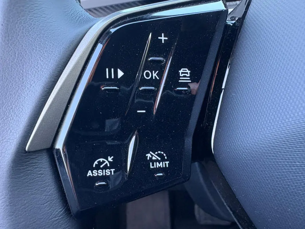 Gros plan sur les commandes noires du volant du Peugeot 5008 Hybrid 2025, avec boutons d'assistance et limitation de vitesse.