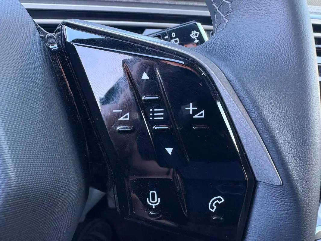 Gros plan sur les commandes tactiles noires à gauche du volant du Peugeot 5008 bleu foncé Hybrid 2025.