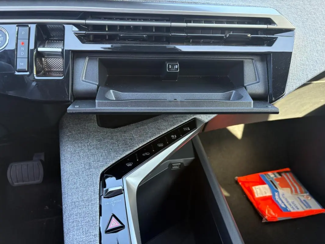 Vue intérieure du tableau de bord côté passager du Peugeot 5008 bleu foncé 2025, avec boîte automatique et rangement ouvert.