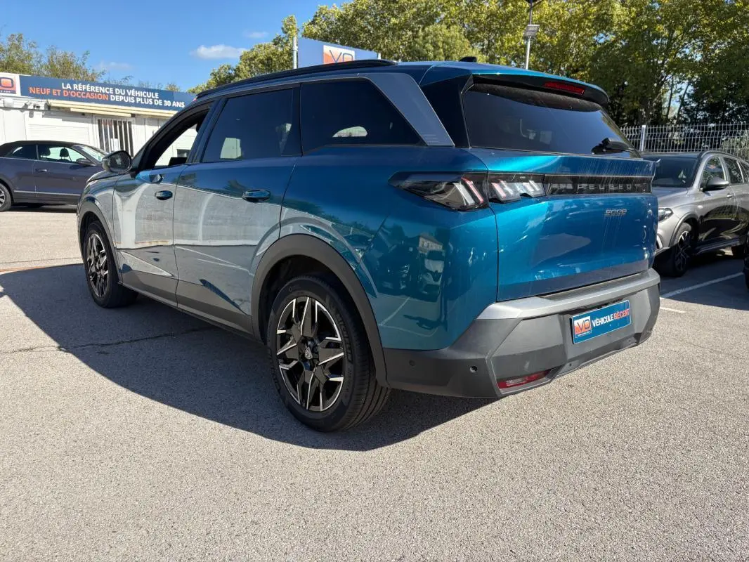 Vue 3/4 arrière droite d’un Peugeot 5008 Hybrid bleu foncé 2025 avec feux arrière distinctifs et jantes noires stylisées.