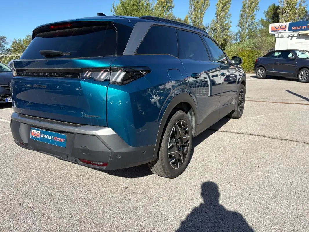 Vue 3/4 arrière droite d’un Peugeot 5008 Hybrid bleu foncé 2025 avec feux arrière distinctifs et jantes noires.
