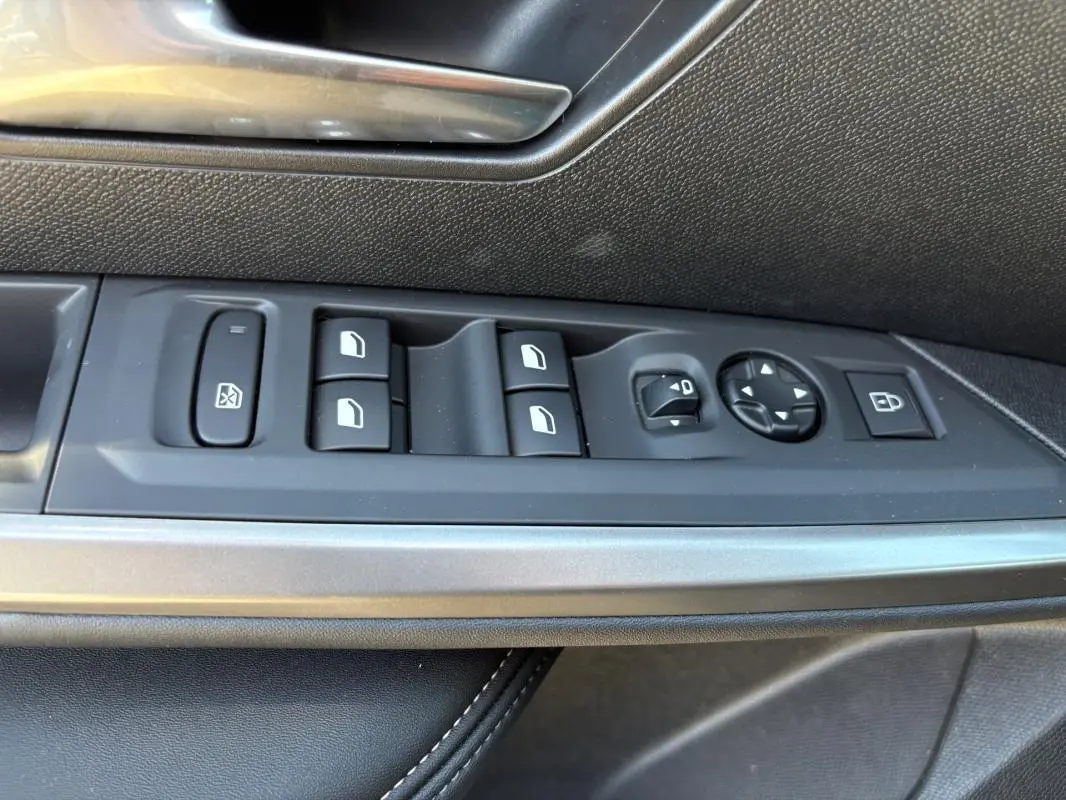 Gros plan sur les commandes de lève-vitres et rétroviseurs côté gauche d’un Peugeot 5008 bleu foncé 2025 Hybrid Allure.