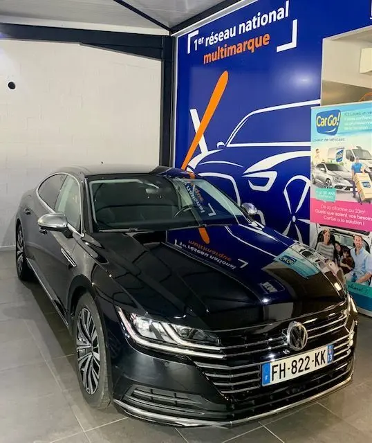Volkswagen Arteon noir 2019 en 3/4 avant droit, avec calandre chromée et phares LED allumés dans un showroom.