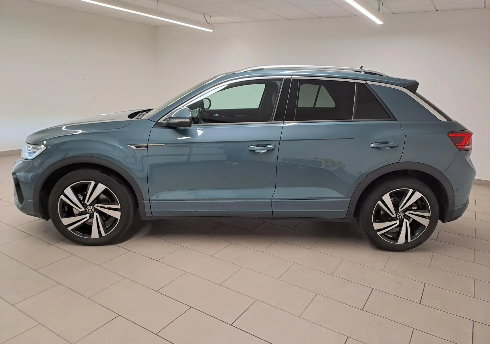 Volkswagen T-Roc 1.5 TSI R-Line bleu pétrole vu de profil côté gauche en intérieur, jantes alliage distinctives.