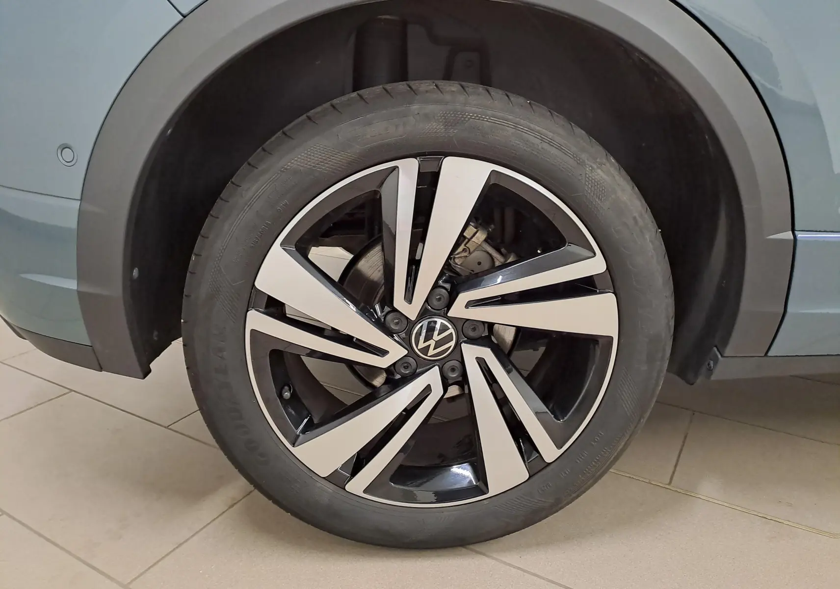 Gros plan sur la roue avant droite du Volkswagen T-Roc bleu pétrole, mettant en valeur la jante alliage bicolore au design moderne.