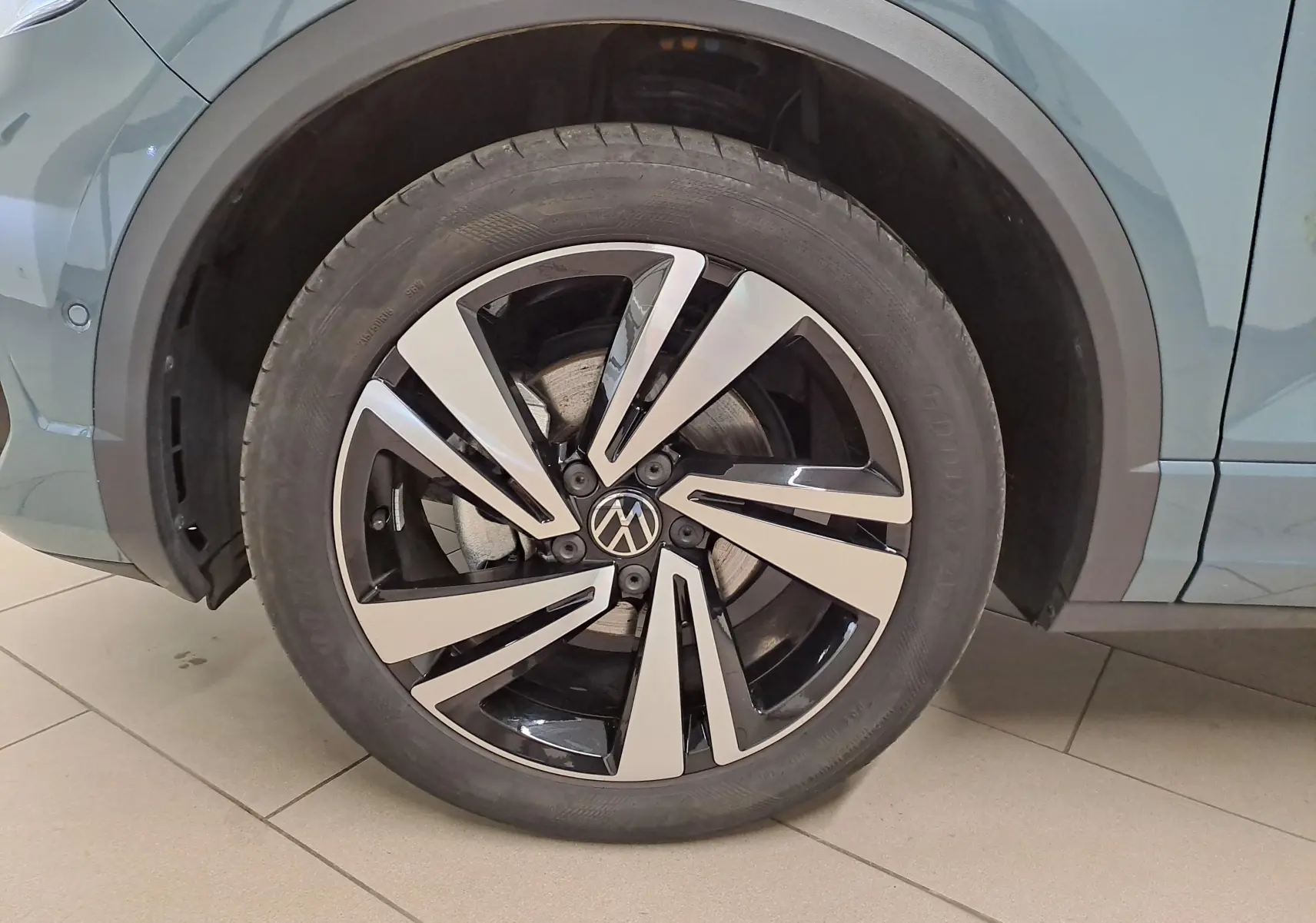 Gros plan sur la roue avant gauche du Volkswagen T-Roc bleu pétrole, mettant en valeur la jante alliage bicolore au design moderne.