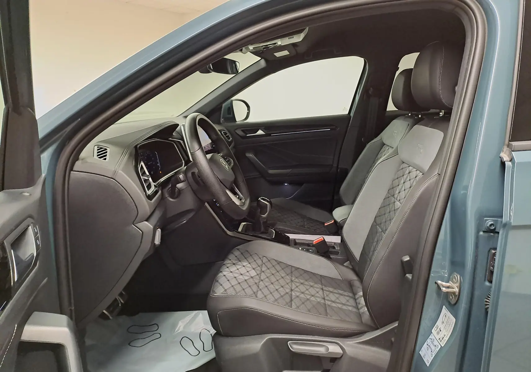 Vue intérieure côté conducteur du Volkswagen T-Roc bleu pétrole 2025, sièges avant R-Line avec surpiqûres et volant cuir.