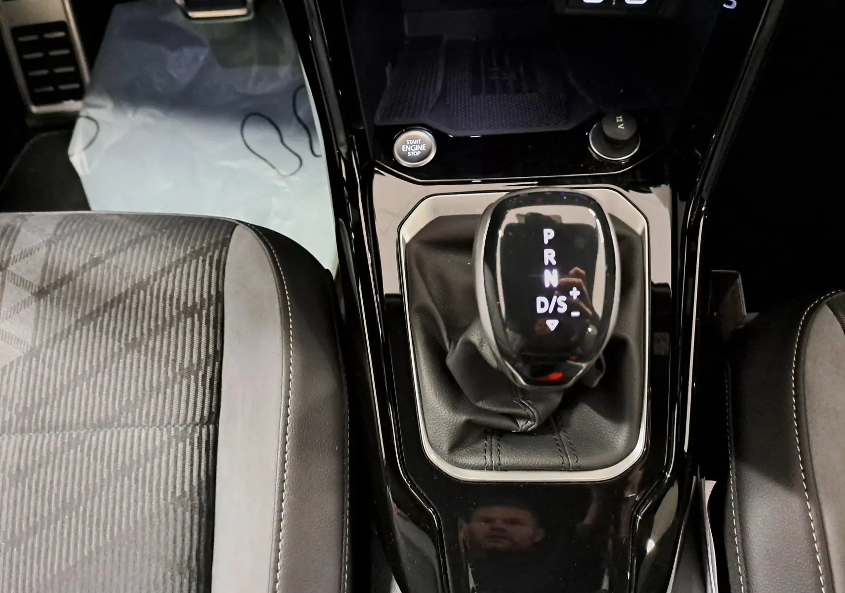 Vue rapprochée de la console centrale du Volkswagen T-Roc 1.5 TSI 150 DSG7, avec levier de vitesses automatique et sièges tissu noir.