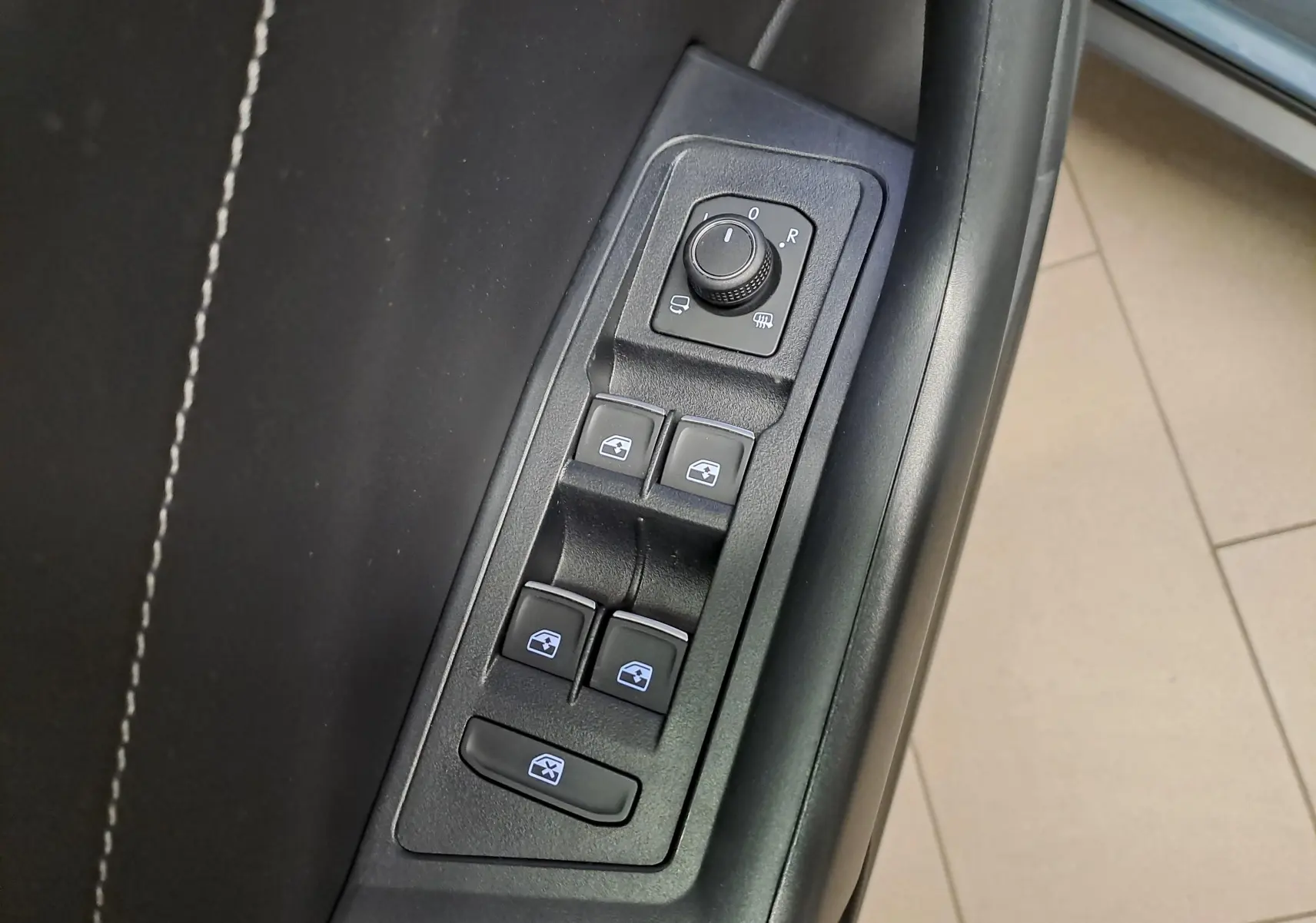 Gros plan sur les commandes de lève-vitres et réglage des rétroviseurs côté conducteur du Volkswagen T-Roc 1.5 TSI bleu pétrole 2025.