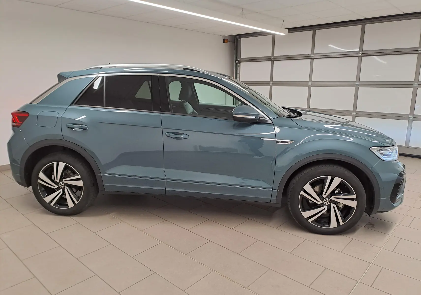 Vue de profil côté gauche du Volkswagen T-Roc 1.5 TSI R-Line bleu pétrole avec jantes alliage distinctives.