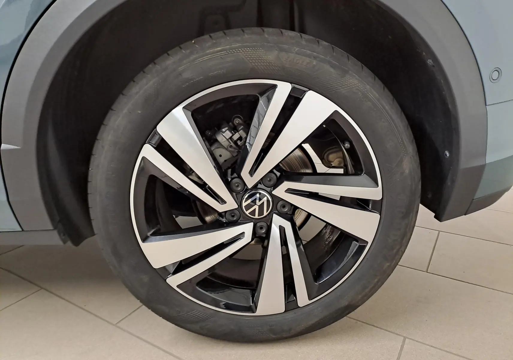 Gros plan sur la roue avant droite du Volkswagen T-Roc bleu pétrole 2025 avec jante alliage bicolore au design moderne.