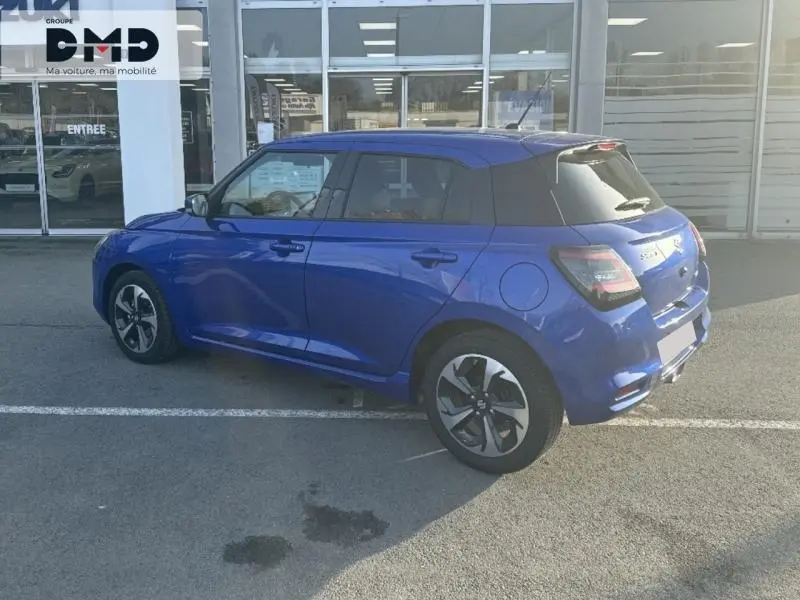 Suzuki Swift 1.2 Hybrid 83ch Pack en bleu Frontier Pearl, vue 3/4 arrière côté gauche sur parking extérieur.