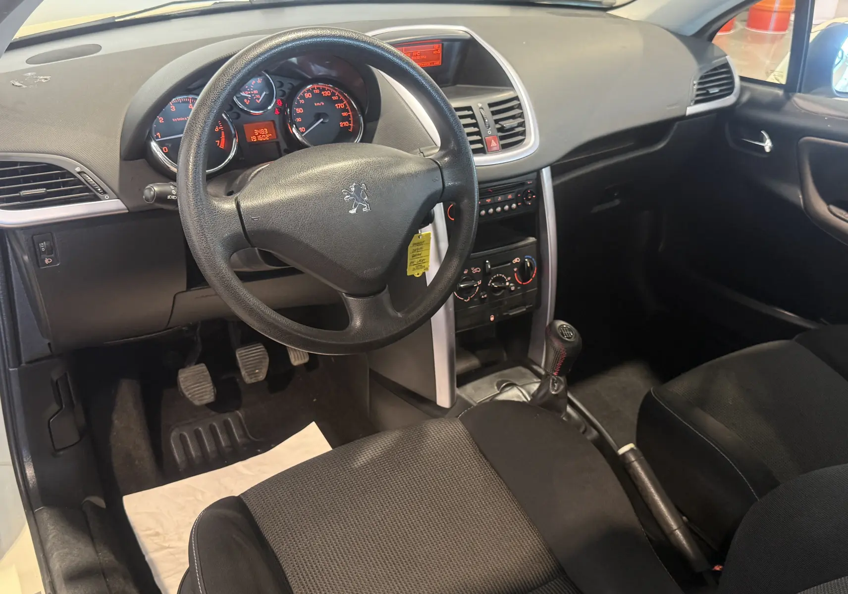 Vue intérieure côté conducteur du Peugeot 207 CC beige de 2007, montrant le volant, tableau de bord et levier de vitesse manuel.