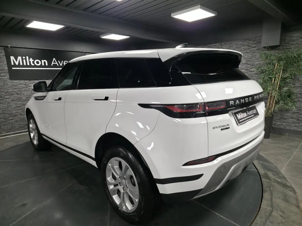 Vue 3/4 arrière droite d'un Range Rover Evoque blanc avec toit noir et jantes argentées en showroom.