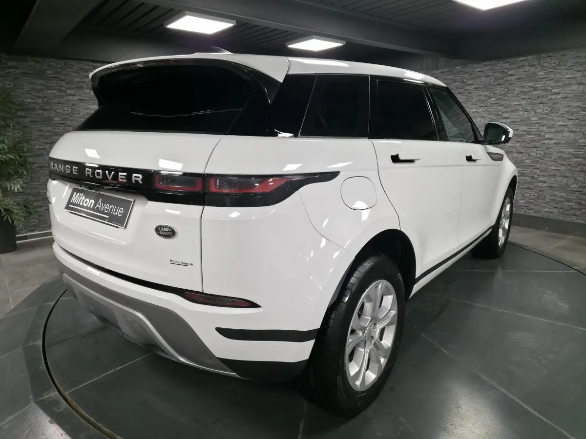 Vue 3/4 arrière droit d'un Range Rover Evoque blanc avec toit noir et jantes 18 pouces dans un showroom.
