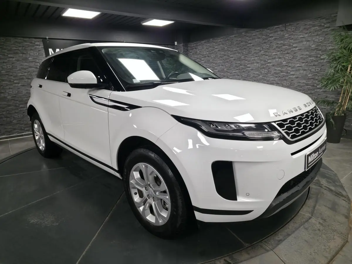 Vue 3/4 avant droite d'un Range Rover Evoque blanc avec calandre noire et jantes argentées en intérieur showroom.