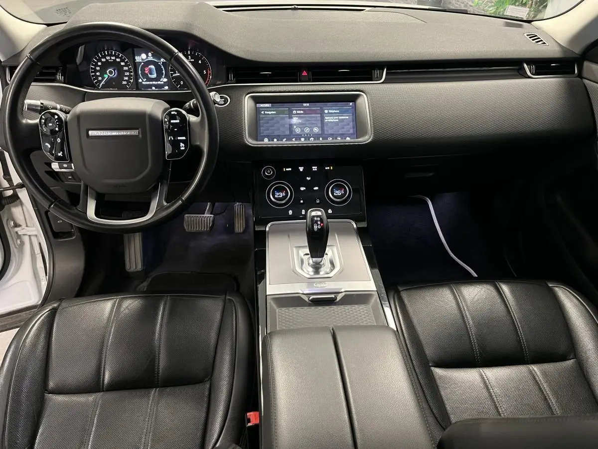 Vue intérieure avant du Range Rover Evoque 2020, sièges cuir noirs, tableau de bord avec écran tactile et volant multifonction.