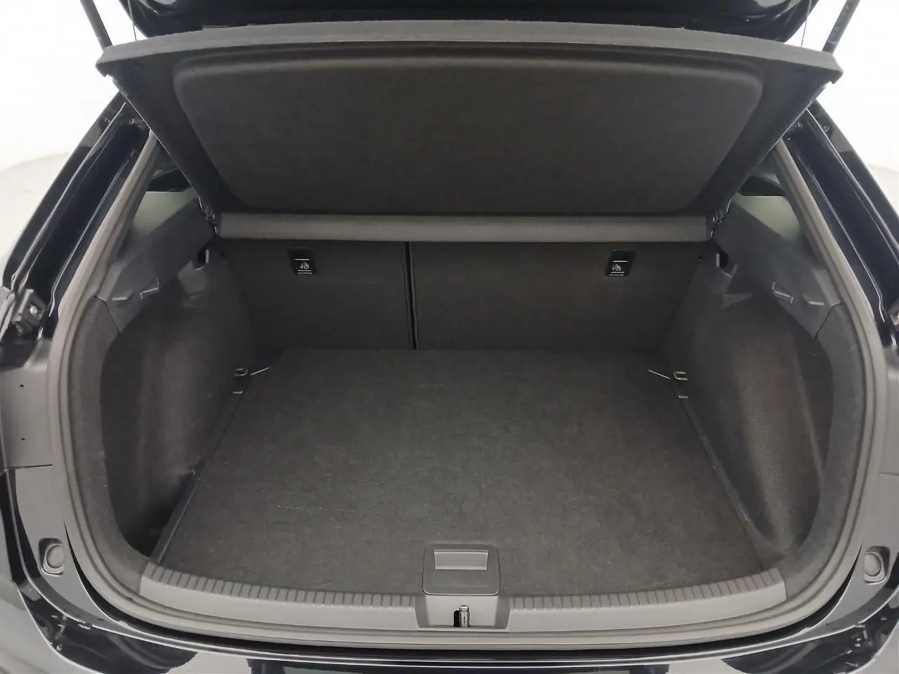 Coffre ouvert vu de l'arrière d'un Volkswagen Taigo noir intense nacré, espace de chargement vide et tapis noir.