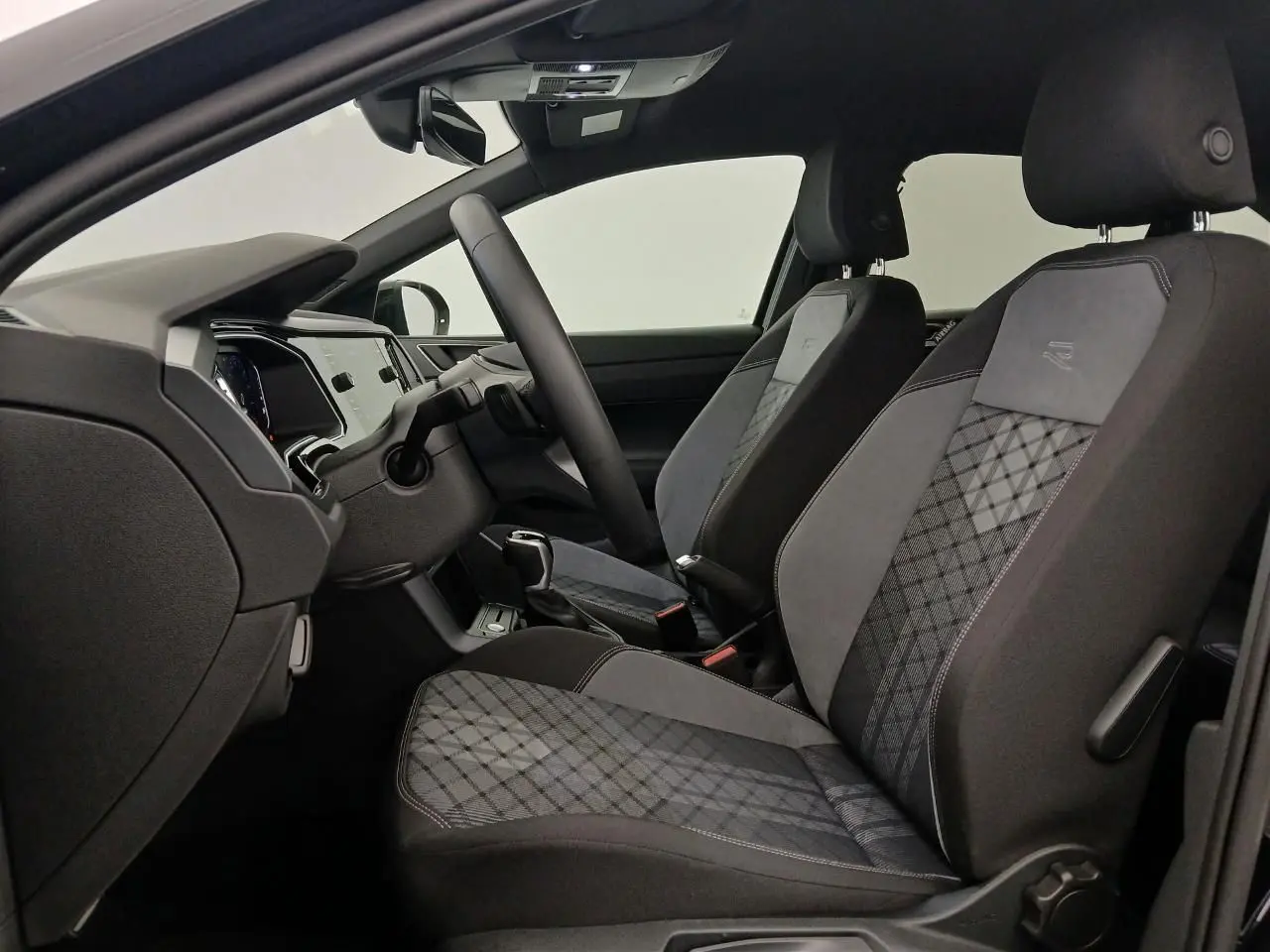 Vue intérieure côté gauche du Volkswagen Taigo R-Line 2025, sièges avant sport en tissu gris à motifs géométriques.