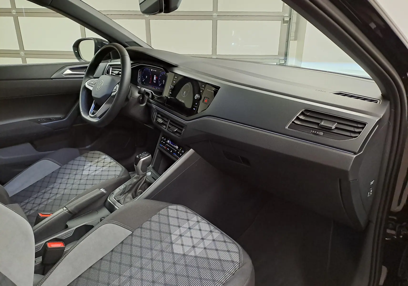 Intérieur du Volkswagen Taigo 1.5 TSI R-Line 2025, vue côté conducteur, sièges tissu gris à motifs et tableau de bord noir.