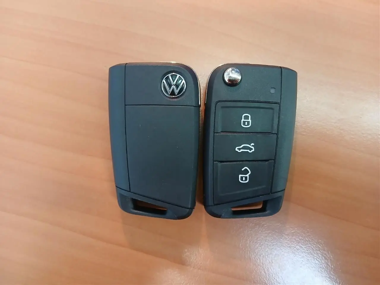 Vue rapprochée de deux clés noires Volkswagen avec boutons de verrouillage et logo sur fond bois clair.