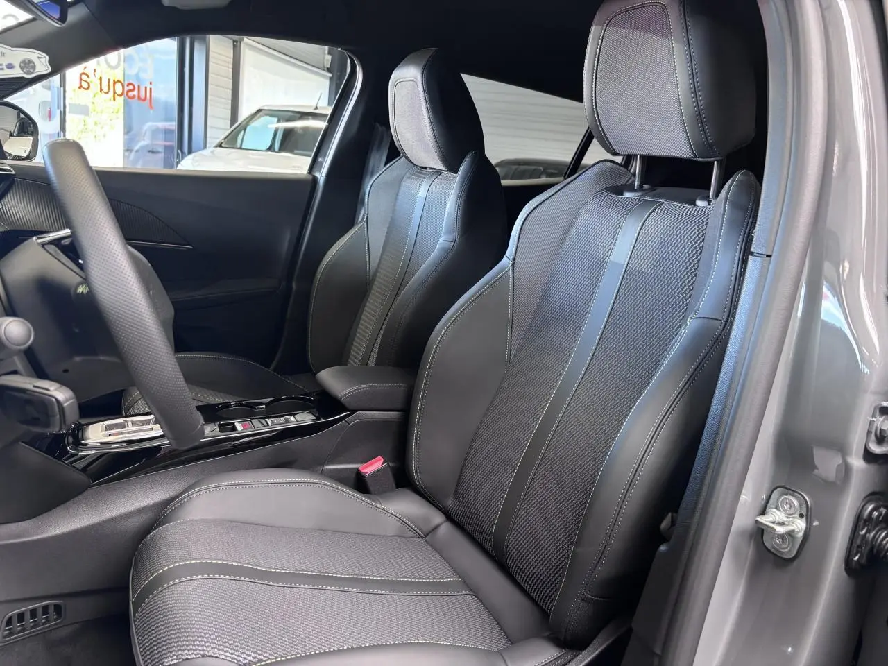 Vue intérieure côté conducteur du Peugeot 2008 gris selenium, mettant en valeur les sièges bi-matière avec surpiqûres vertes et volant compact cuir.
