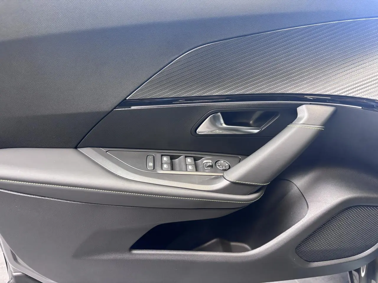 Détail de la porte avant gauche du Peugeot 2008 gris selenium, avec commandes de vitres et insert carbone.