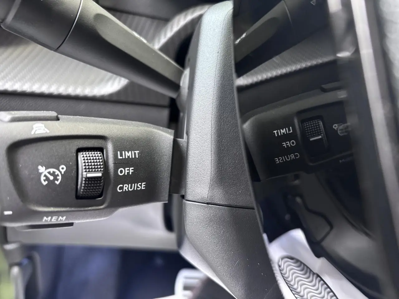 Gros plan sur la commande de régulateur de vitesse noire du Peugeot 2008 1.2i Hybrid, intérieur gris selenium.