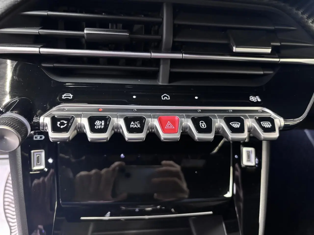 Gros plan sur la console centrale noire brillante du Peugeot 2008 1.2i Hybrid avec boutons argentés et rouge d'alerte.
