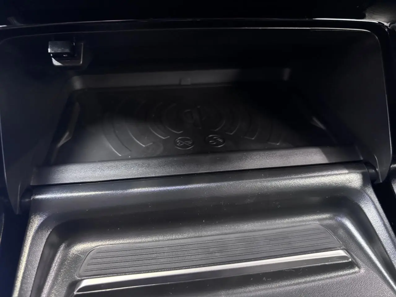 Gros plan sur le compartiment de rangement avant avec chargeur sans fil dans le Peugeot 2008 gris selenium.