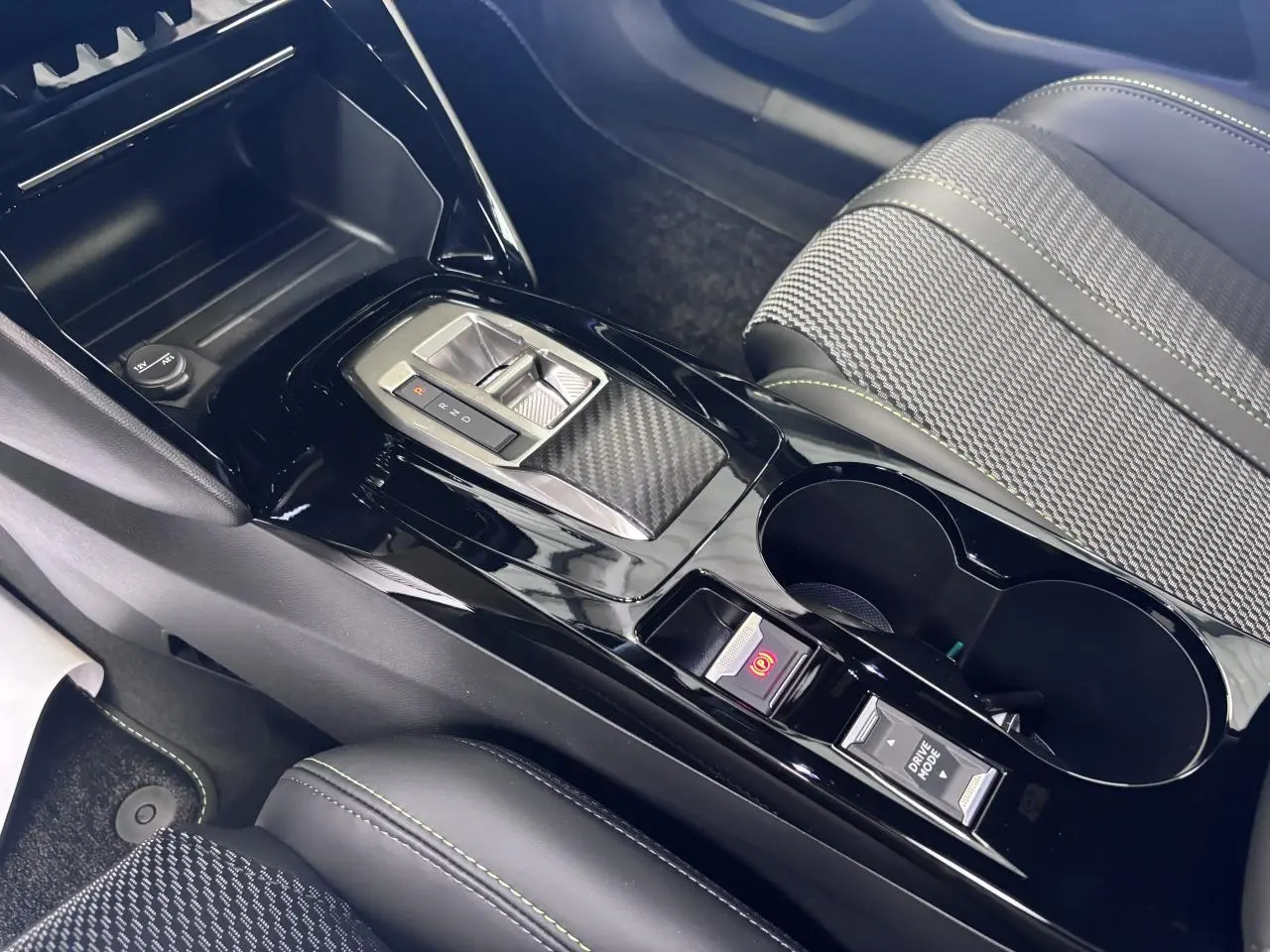 Vue rapprochée de la console centrale noire brillante avec levier de vitesse et siège tissu gris avec surpiqûres vertes Peugeot 2008.