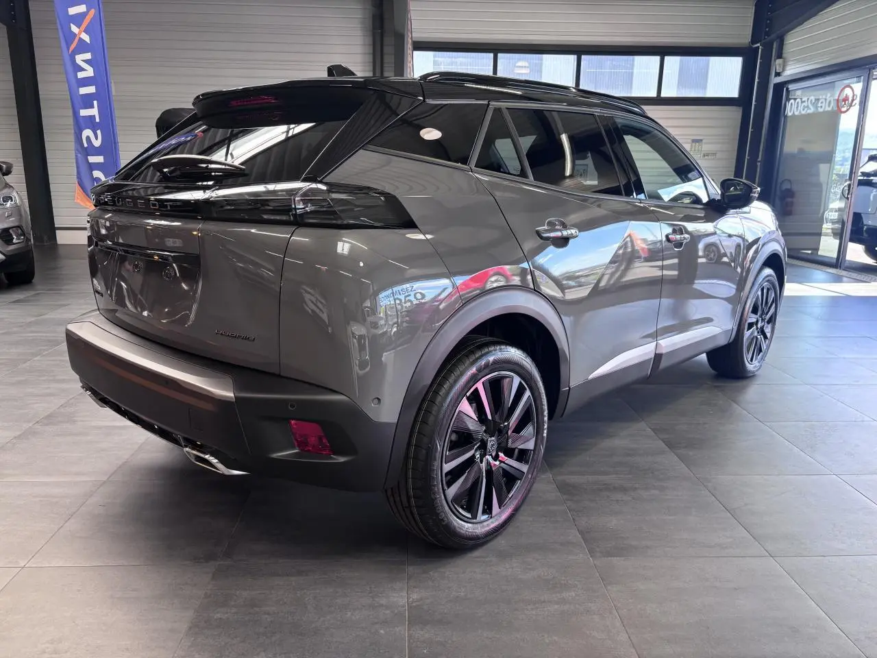 Peugeot 2008 gris selenium en 3/4 arrière droit, jantes alliage bi-ton noir et toit noir brillant visible en showroom.