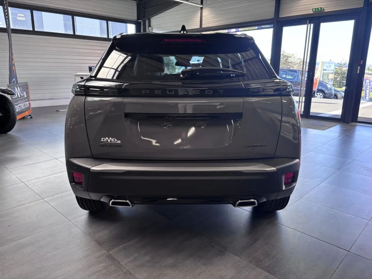 Vue arrière du Peugeot 2008 gris selenium avec double sortie d’échappement chromée et toit noir brillant en showroom.