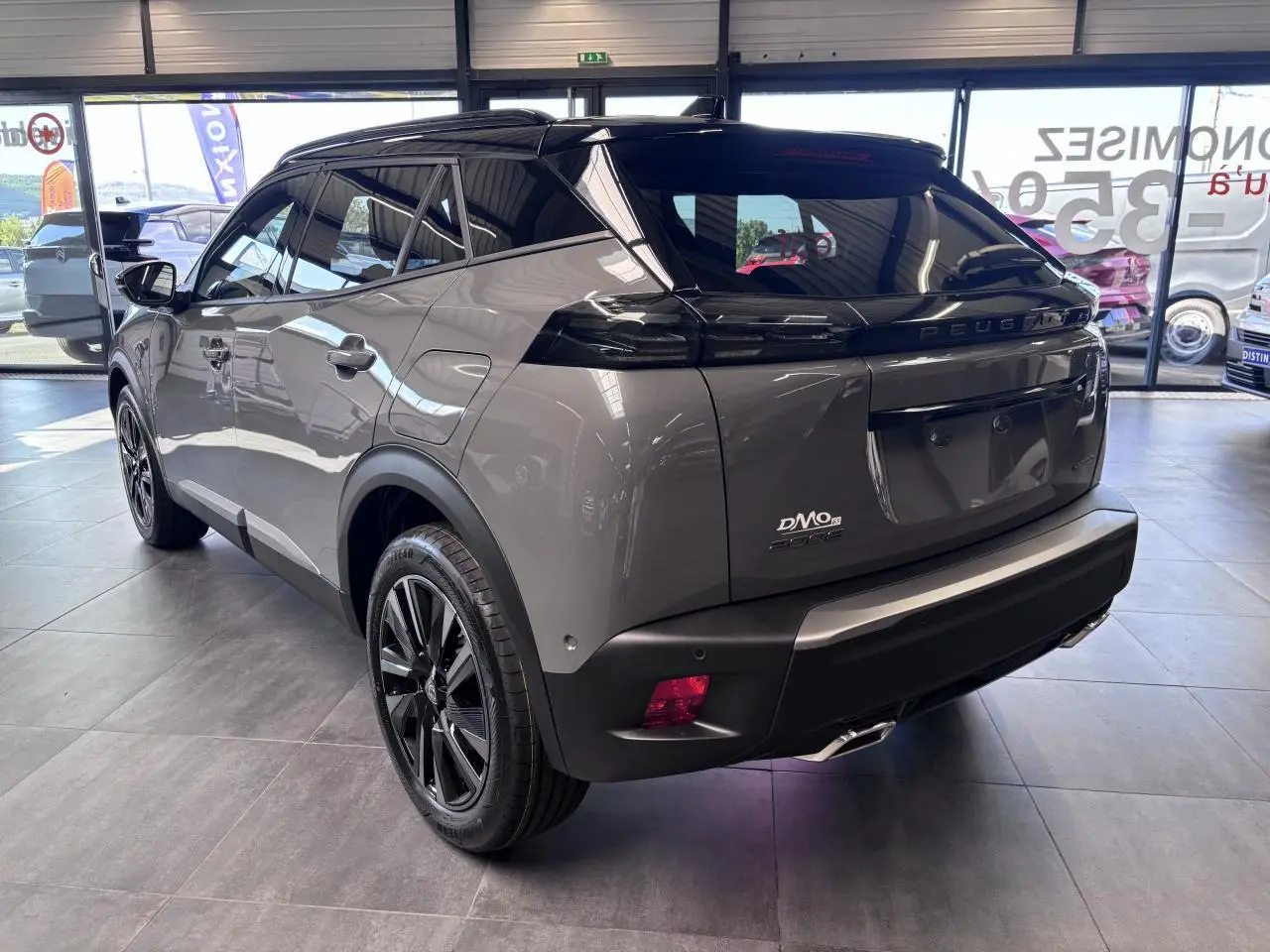Vue 3/4 arrière droite du Peugeot 2008 gris selenium avec toit noir et jantes alliage bi-ton dans un showroom.