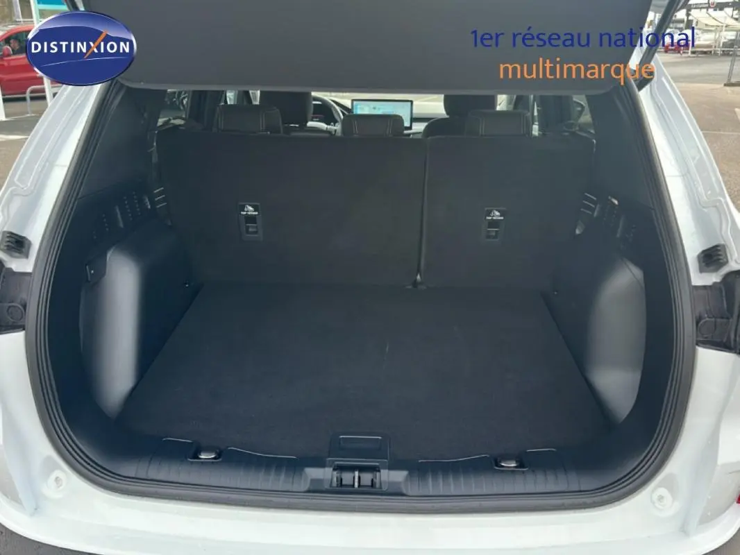Coffre ouvert vu de l'arrière d'un Ford Kuga blanc 2025, avec banquette arrière noire et espace de chargement vide.