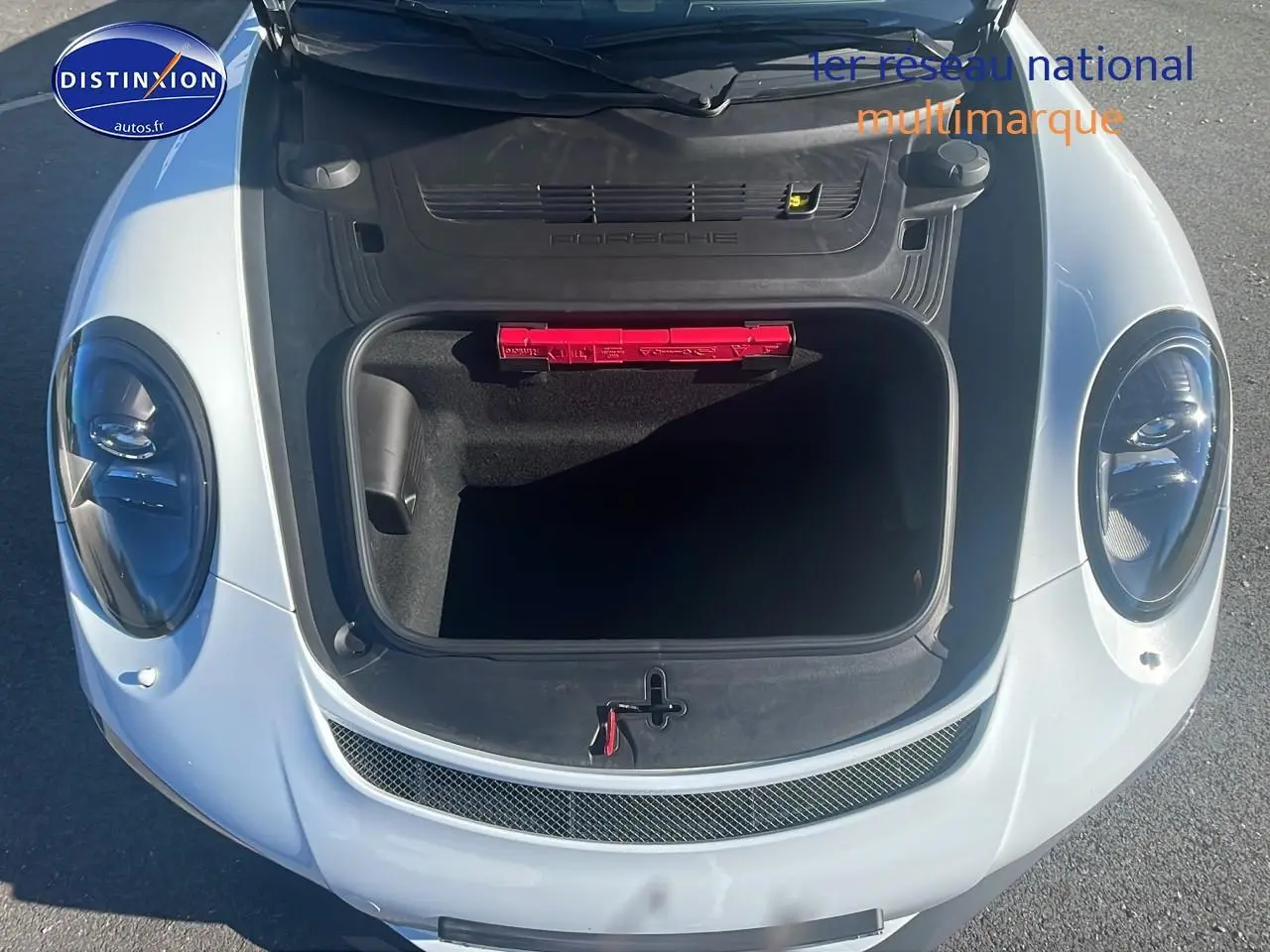 Vue plongeante sur le coffre avant ouvert d'une Porsche 911 GT3 blanche, avec trousse de secours rouge visible.