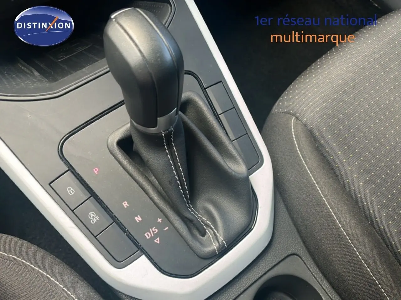 Gros plan sur la commande de boîte automatique noire dans l’habitacle d’un SEAT Arona 2025, siège tissu gris visible.