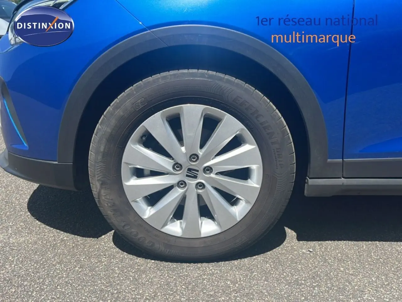 Gros plan sur la roue avant gauche d'un SEAT Arona bleu saphir métal avec jante argentée et partie de la carrosserie visible.