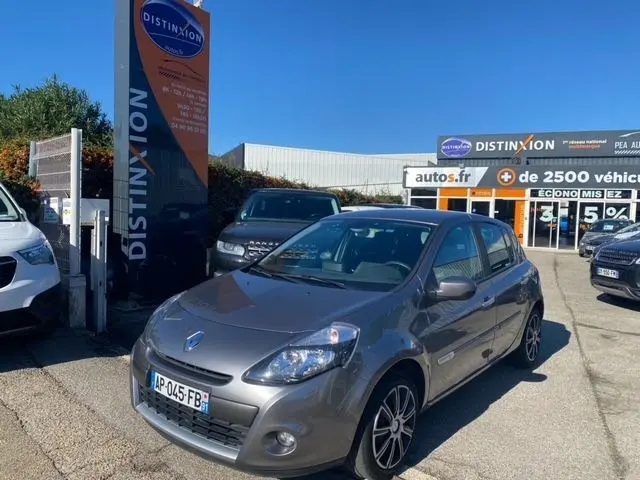 Renault Clio III gris métallisé vue 3/4 avant droit sur un parking devant un concessionnaire Distinxion.