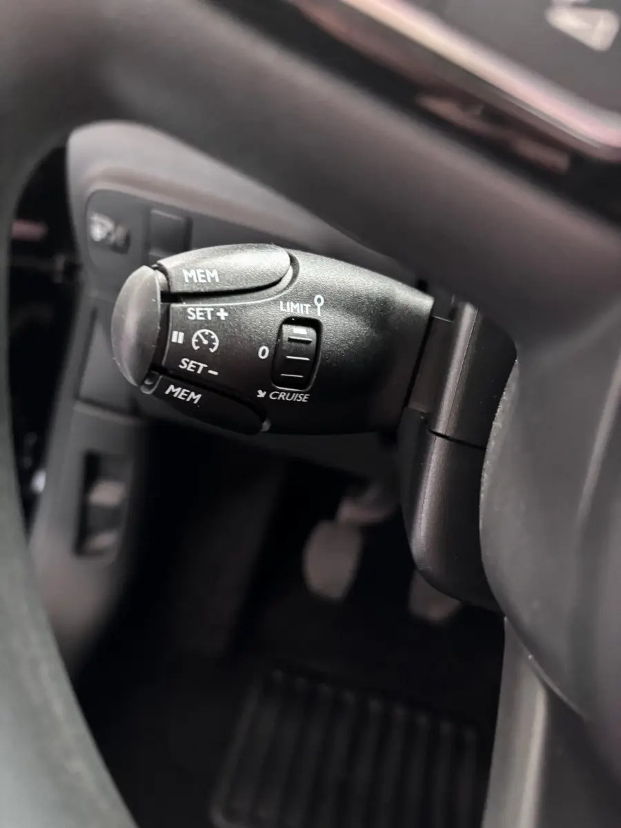 Gros plan sur la commande de régulateur de vitesse à gauche du volant dans l'habitacle noir de la Citroën C3 2024.