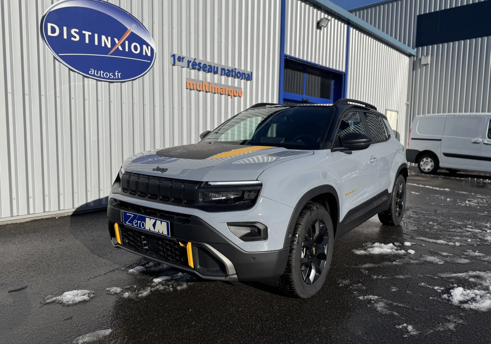 Jeep Avenger Storm Grey en 3/4 avant droit, avec toit noir et accents jaunes sur la calandre et le capot.